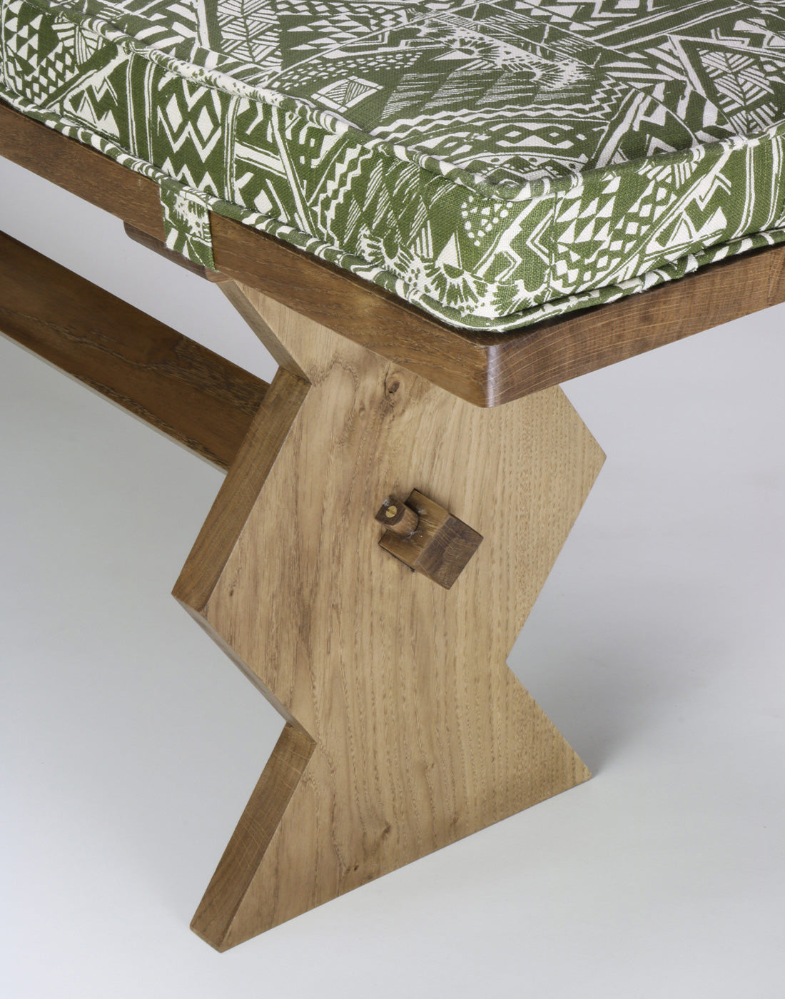 Wooden bench with a green patterned cushion on a white background.
