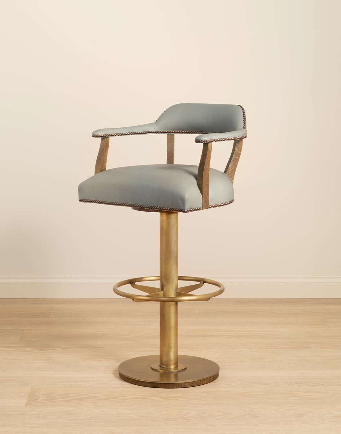 Grey cushioned bar stool with brass base on a wooden floor.