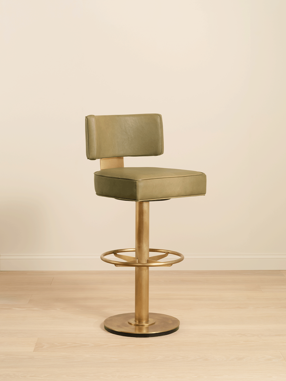 Green bar stool with gold brass base on a beige background.