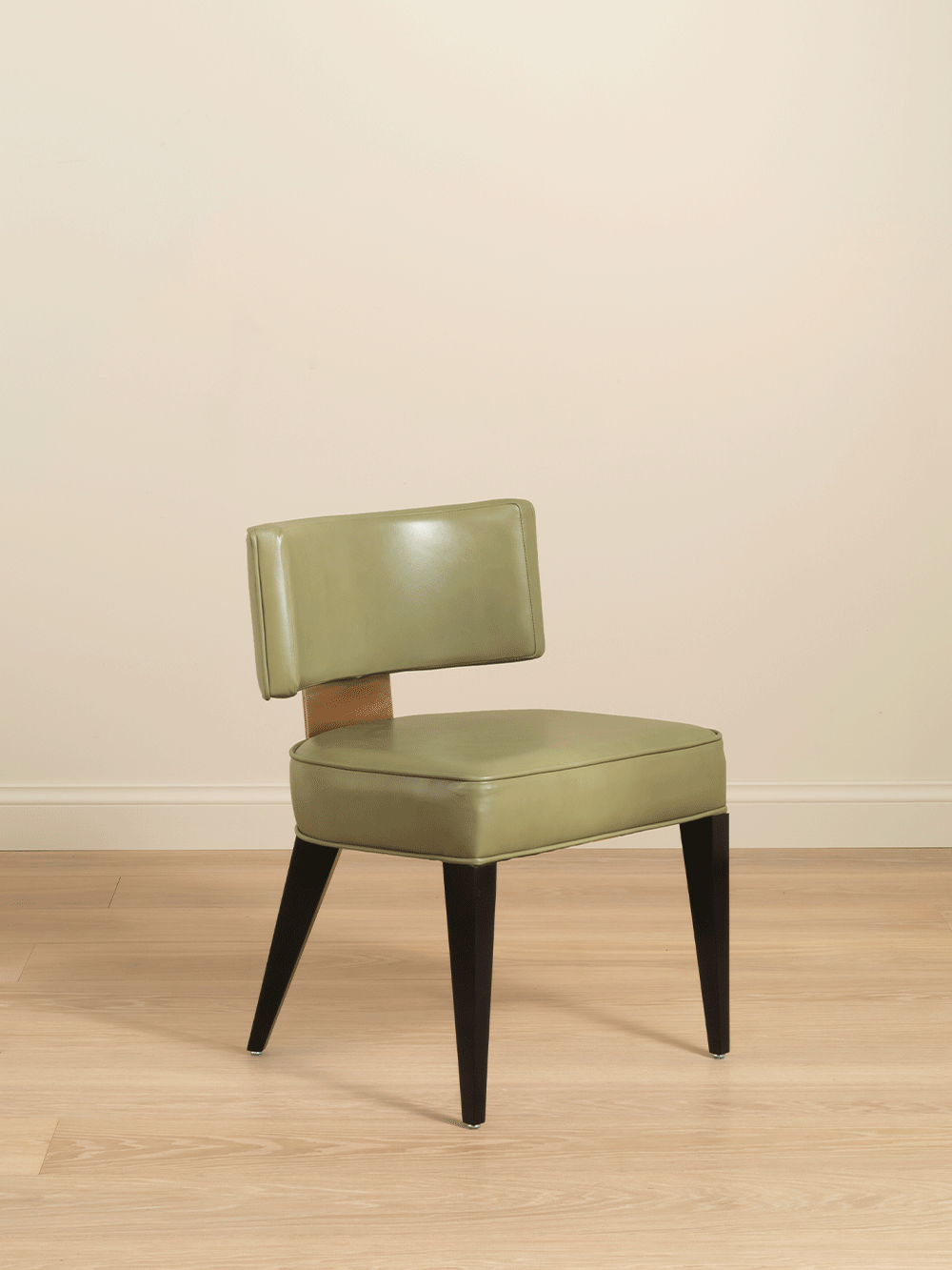 Green chair with black wooden legs on a beige floor and wall.