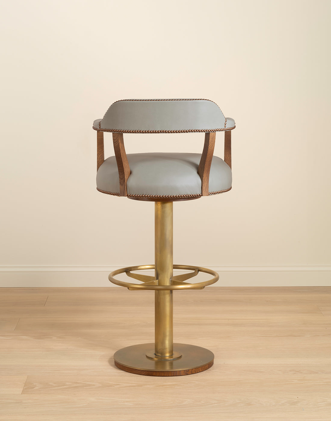 Bar stool with a brass base on a wooden floor against a beige wall.