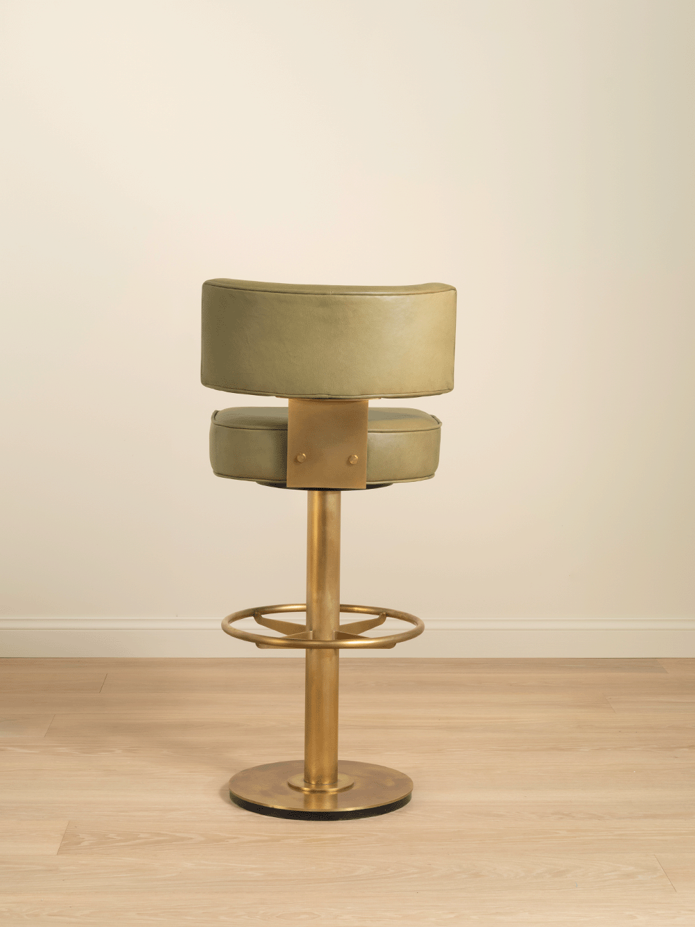 Bar stool with green cushioned seat and gold brass base on a wooden floor.