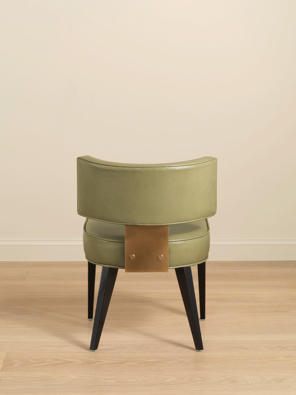 Green chair with black wooden legs on a wooden floor against a beige wall.