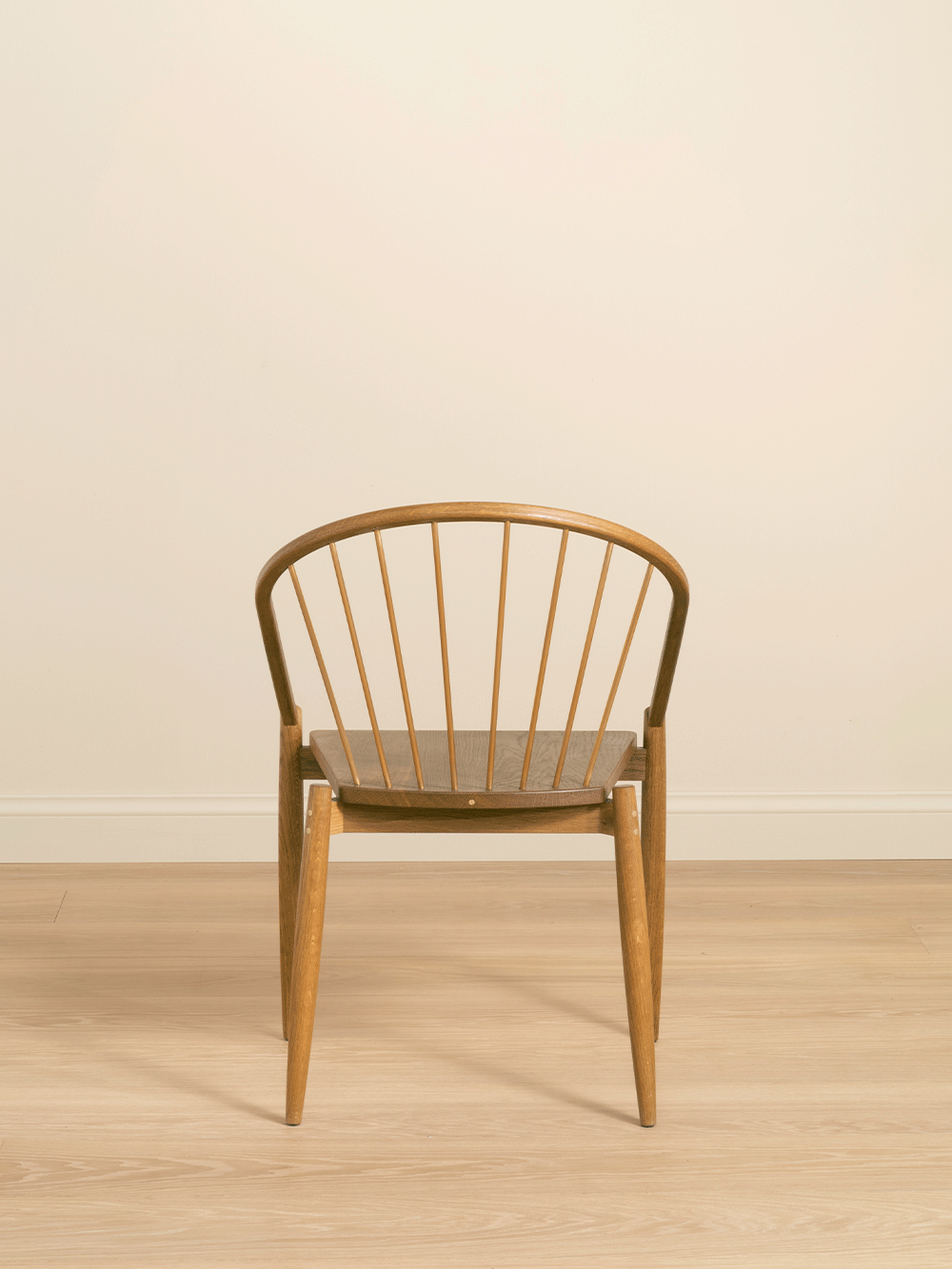 Back of oak chair with brass details on a wooden floor with a beige background.
