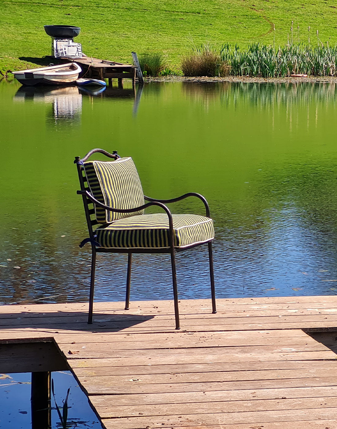 Steel chair with striped cushions on a wooden dock by a calm lake.
