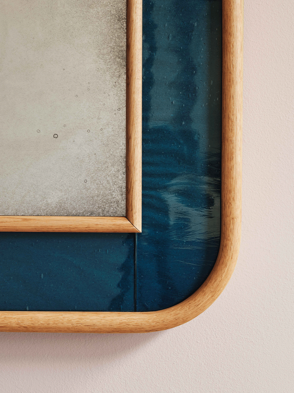 Close-up of mirror with a wooden frame and blue glass on a neutral background.