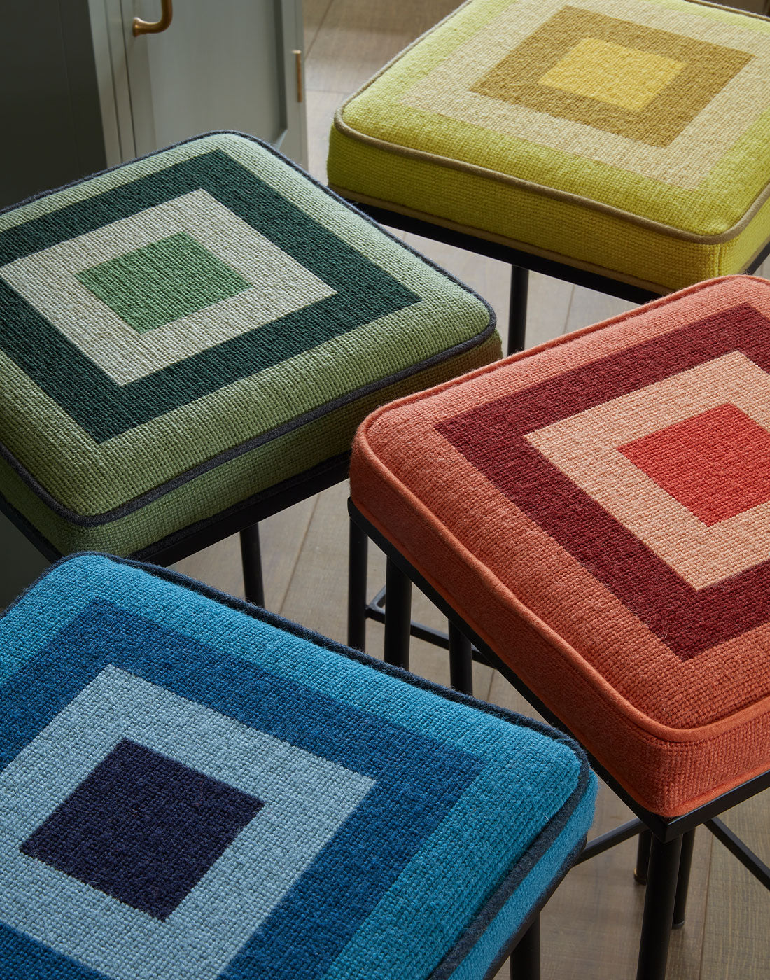 Four colourful bar stools with geometric patterns on a wooden floor.