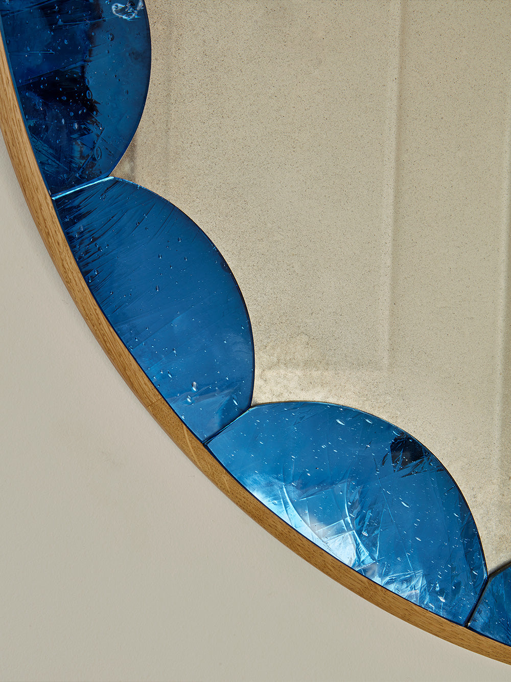 Round mirror with blue cathedral glass from beige wall. 