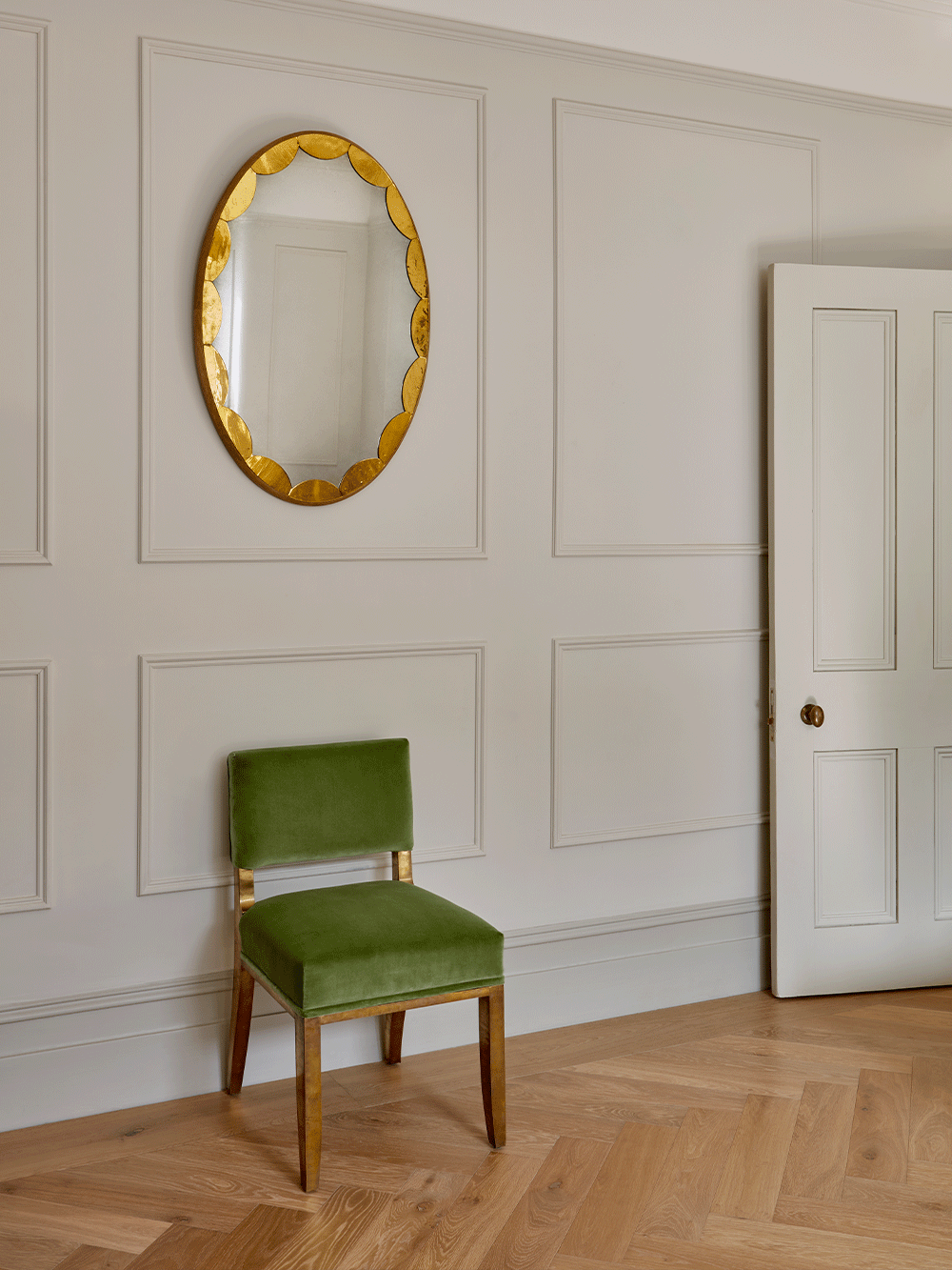 Green chair in a room with a decorative oval mirror on the wall.