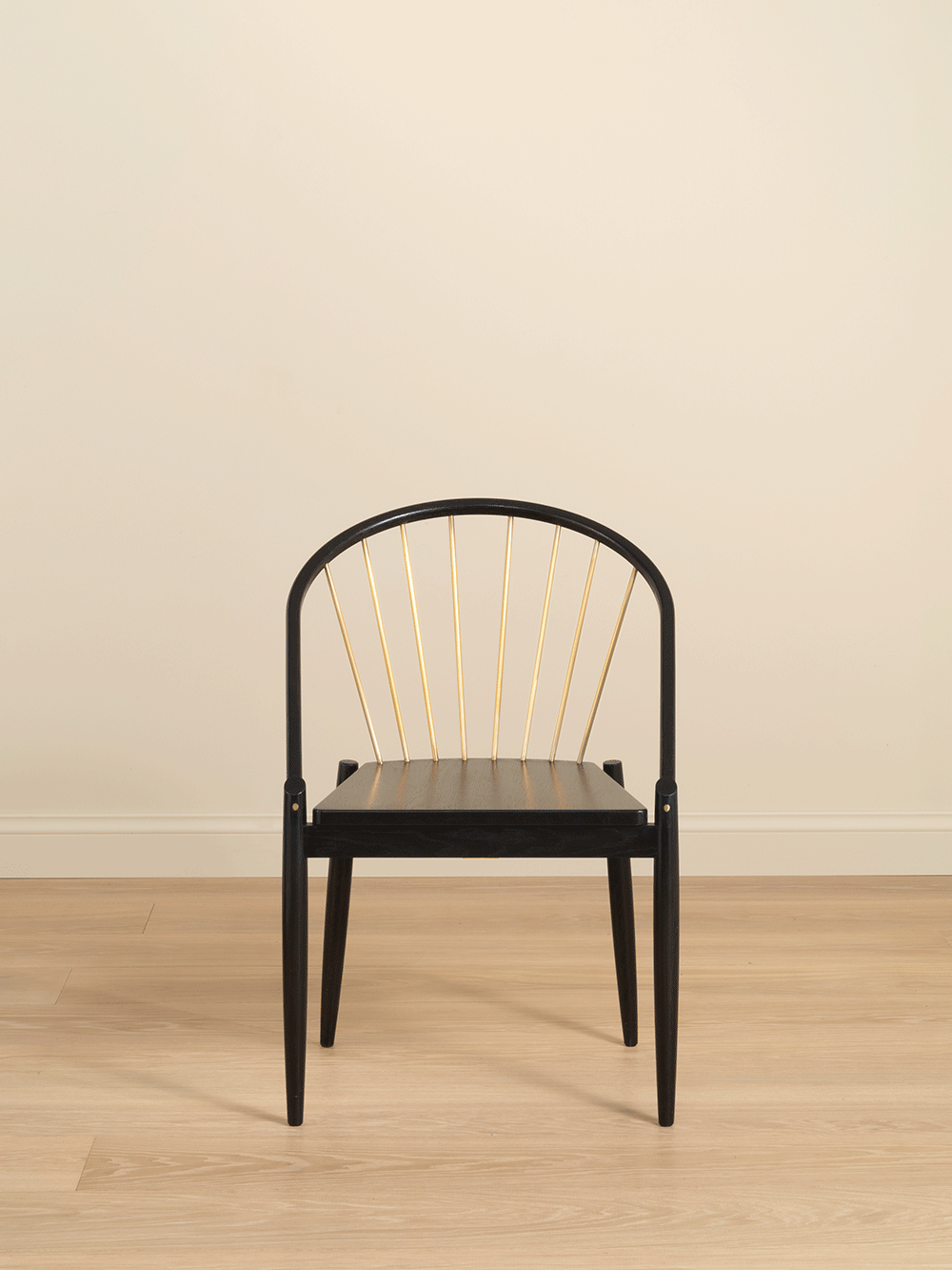 Black chair with brass accents on a wooden floor and beige wall. background