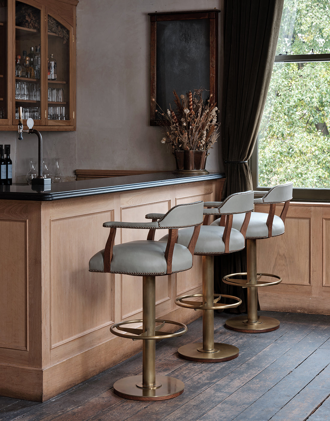 Bar area with wooden cabinets, a chalkboard and bar stools with leather seats and brass bases.