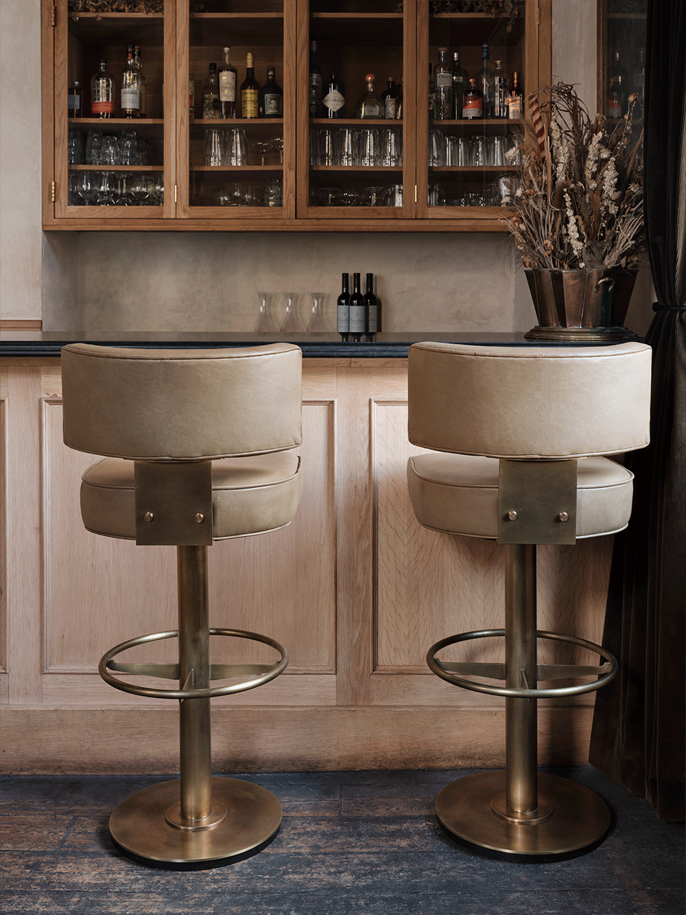 Two bar stools with beige cushioned seats and metal bases in a bar setting.