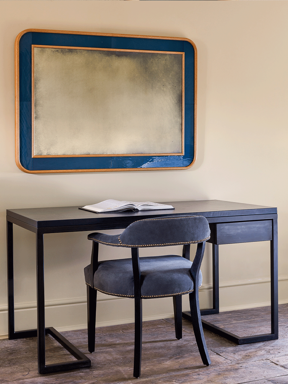 Desk with chair and blue framed mirror on a wall.