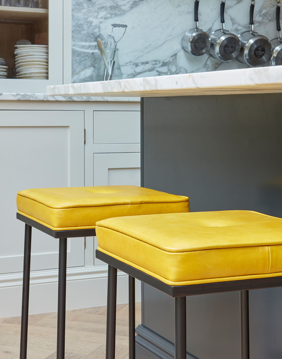 Two yellow bar stools in a kitchen setting with marble countertops and cooking pots.