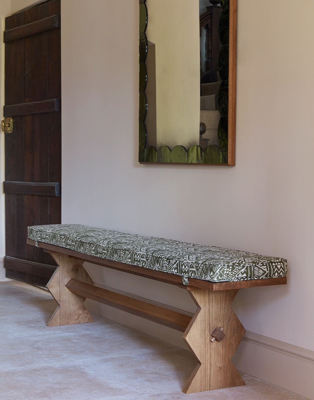 Wooden bench with a patterned cushion against a wall with a mirror.