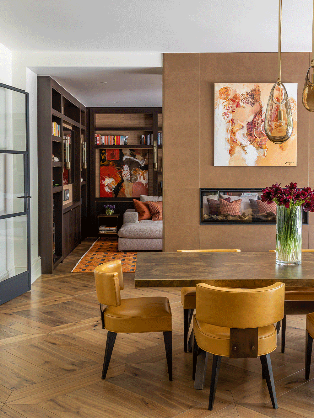 Modern living room with brass dining table and mustard yellow dining chairs, bookshelf and wall art.