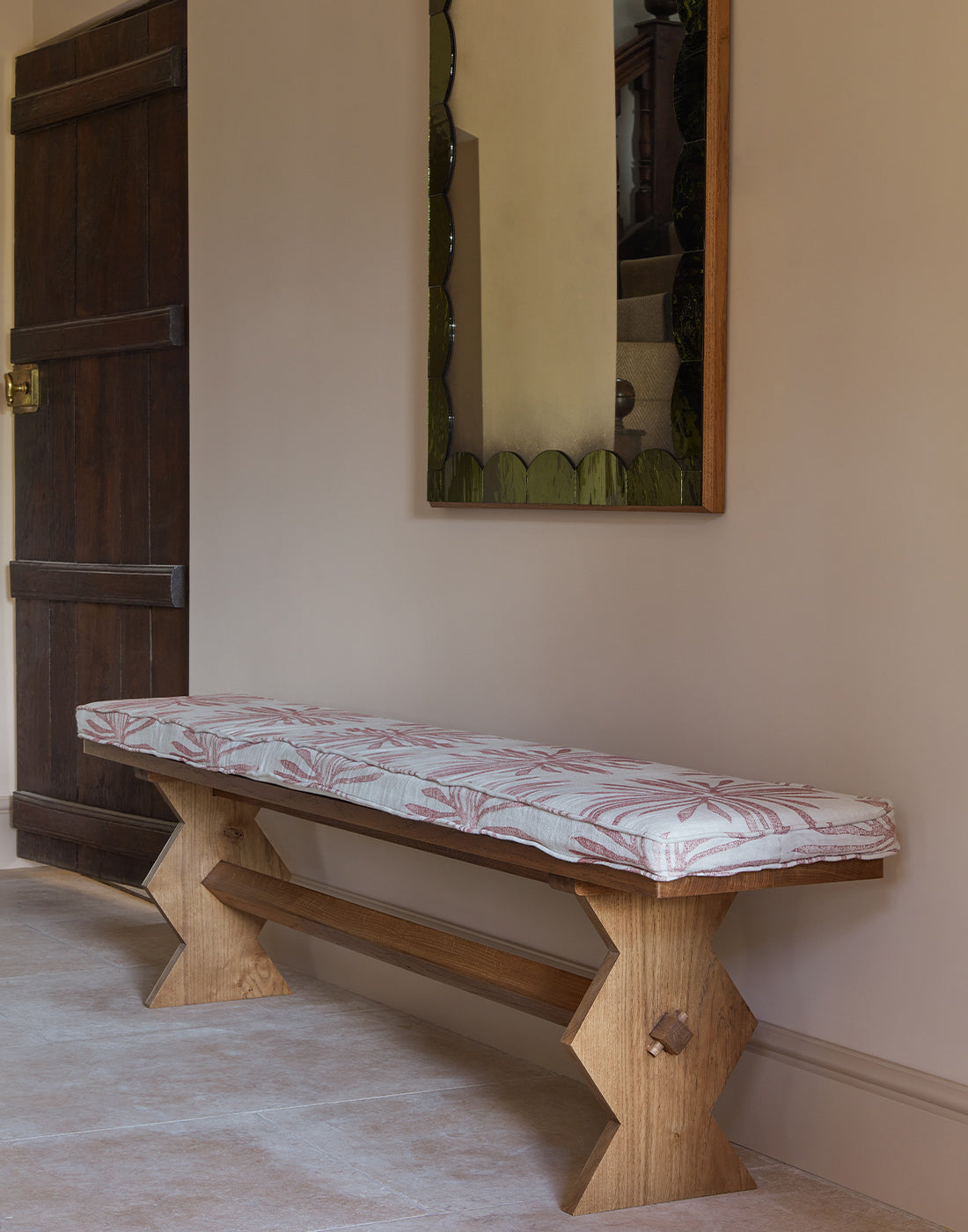 Wooden bench with a patterned cushion against a beige wall with a mirror.