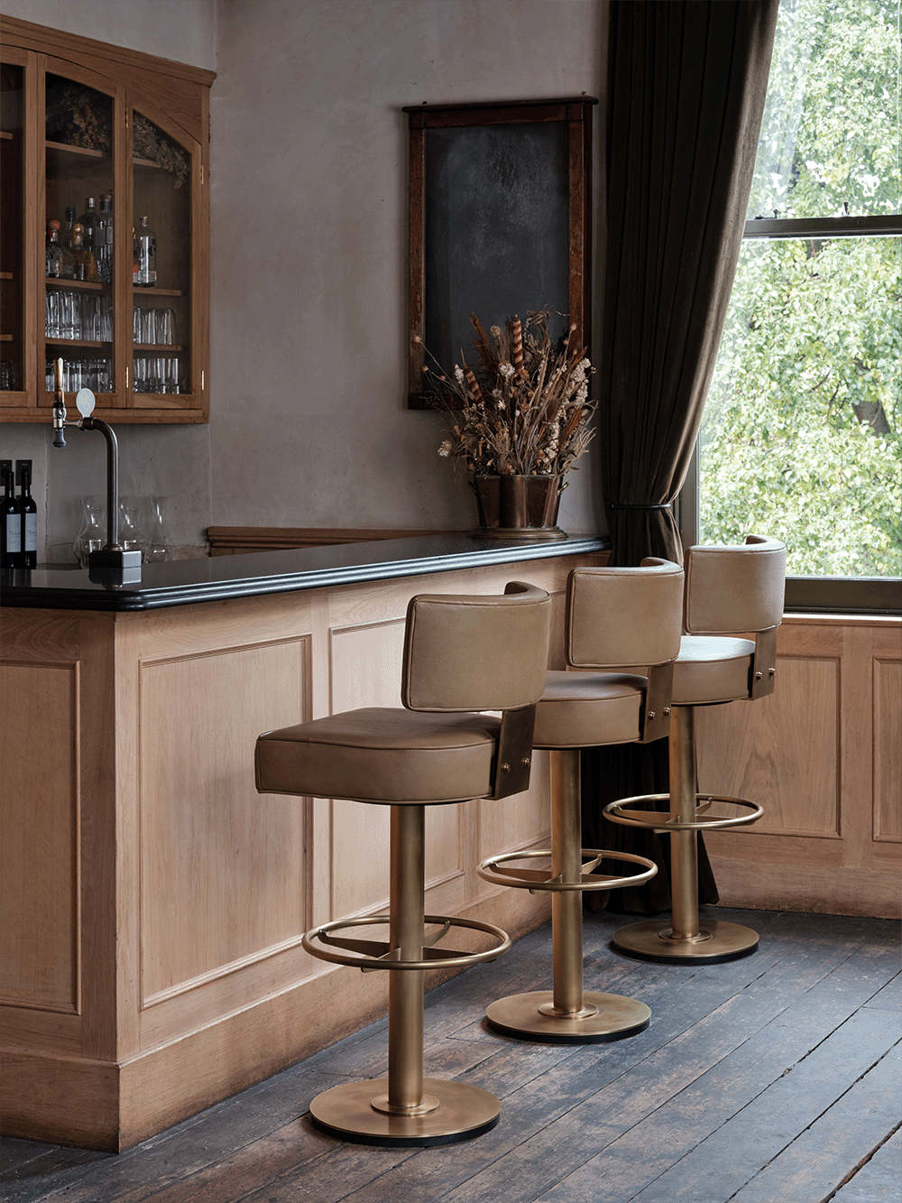 Bar area with wooden cabinets, a bar counter and three brown leather bar stools.