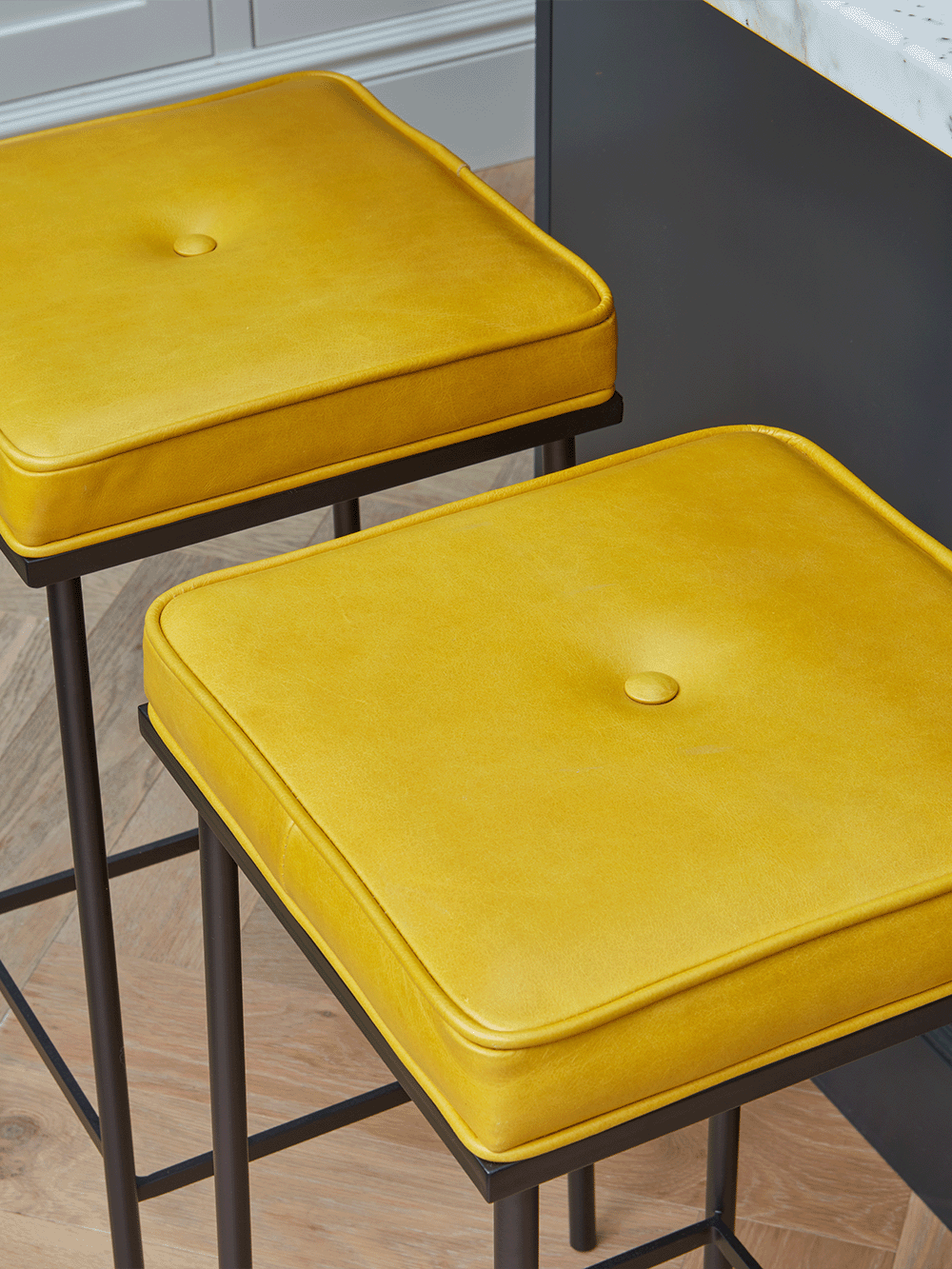 Two yellow bar stools with black metal frames on a wooden floor.