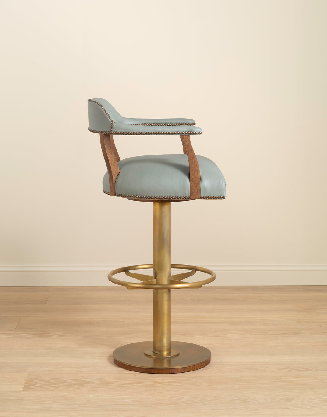 Bar stool with blue cushioned seat and brass metal base on a wooden floor.