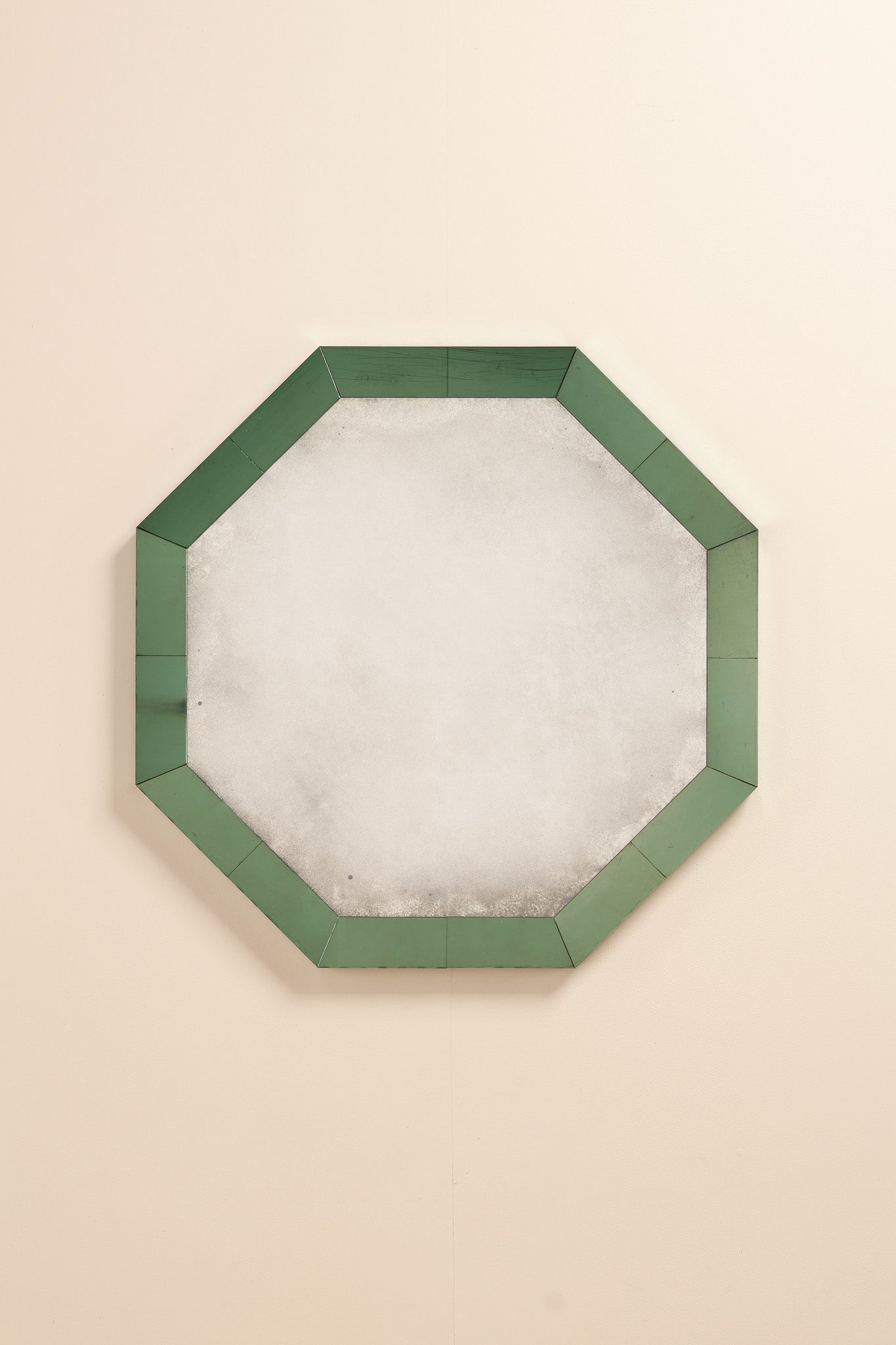 Octagonal wall mirror with a green border on a beige background.  