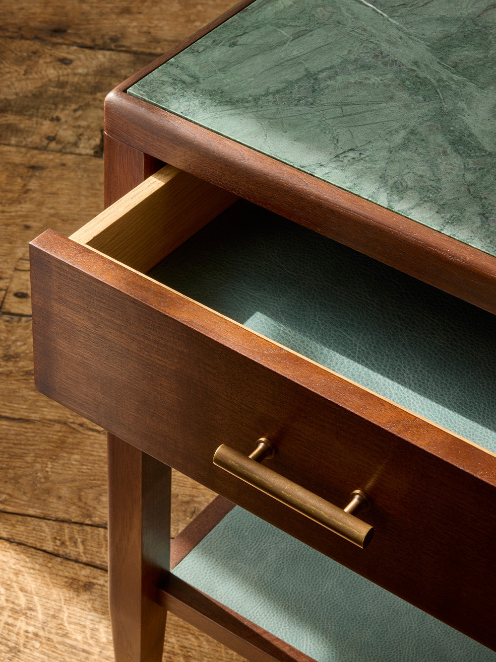 Wooden side table with marble top and open drawer on a wooden floor.
