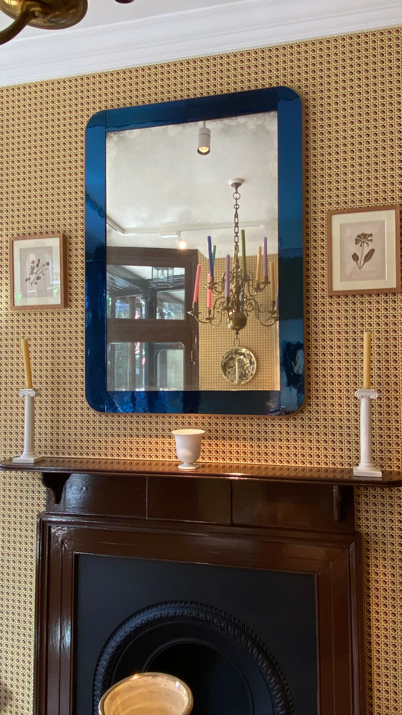 A rectangular wall mirror with a blue frame hanging above a dark wood fireplace mantel.