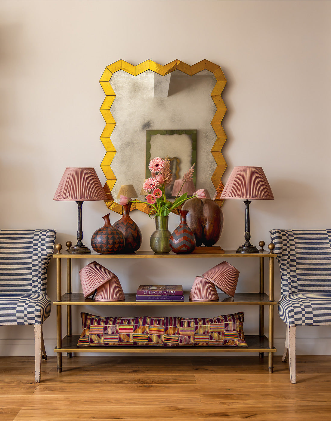 Decorative shelf with a gold mirror, lamps, vases and pillows in a room setting.