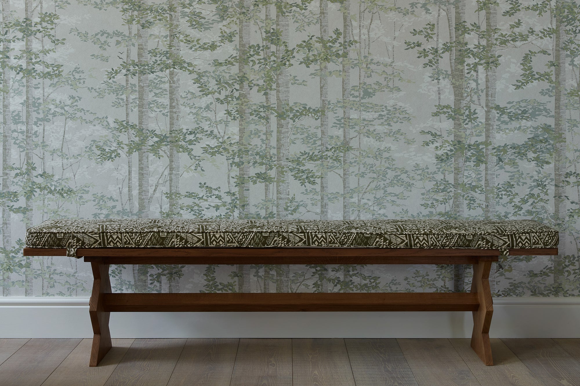 Wooden bench with patterned seat against a wall with forest wallpaper.