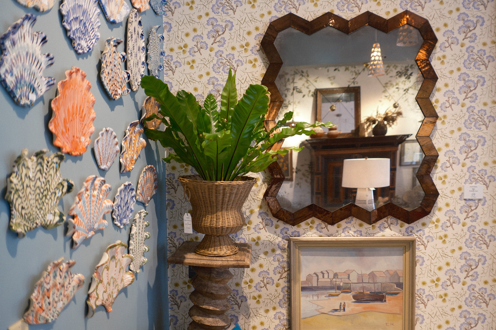 Decorative wall with shell art, a mirror and a plant in a room with floral wallpaper.