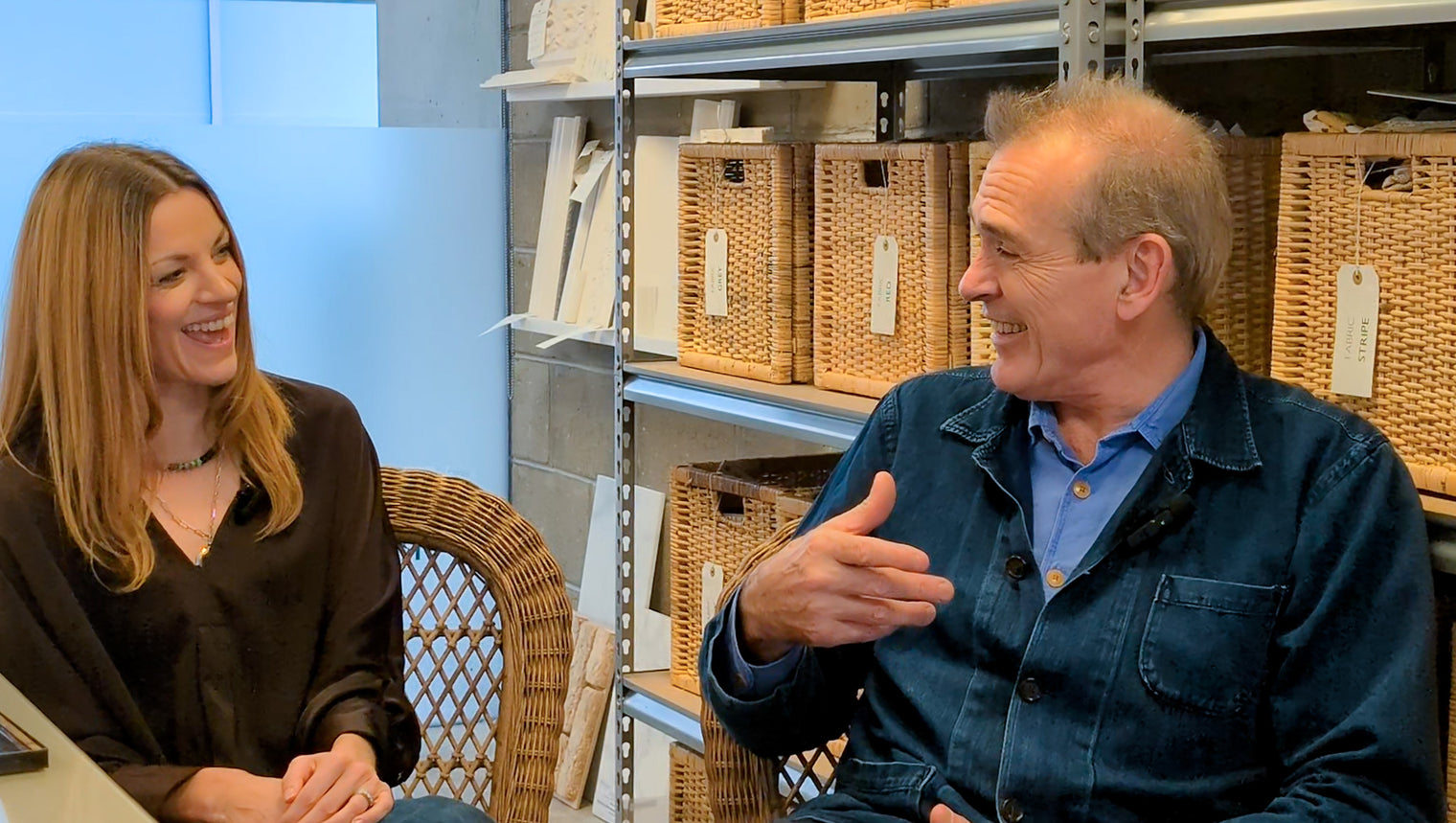 Two people sitting in a room with shelves and wicker baskets.
