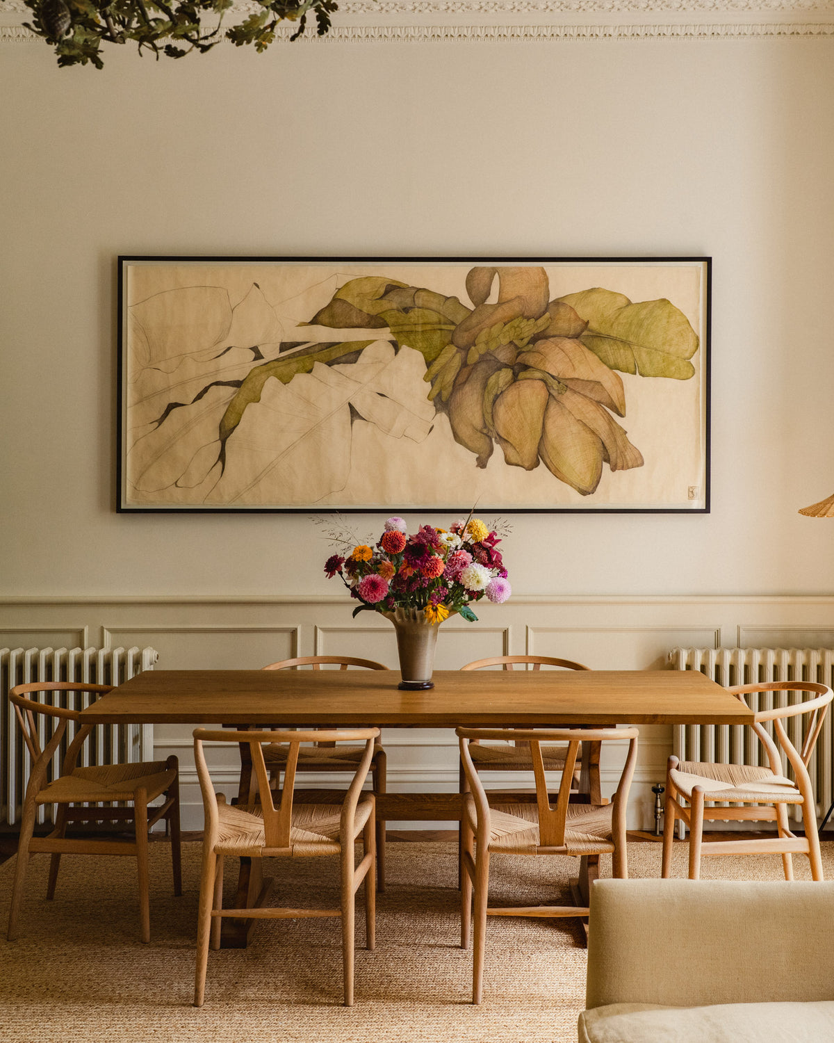 Dining room with wooden table and chairs, floral arrangement and large framed painting on the wall.