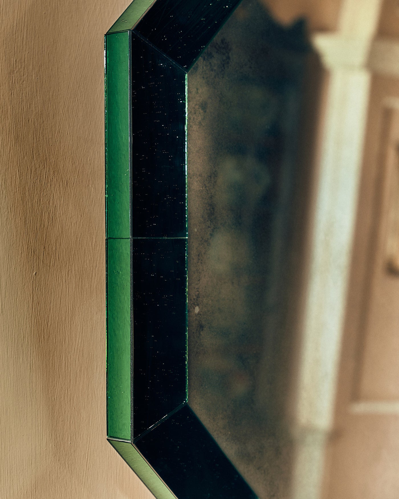 Close-up of green mirror glass frame on a beige wall.