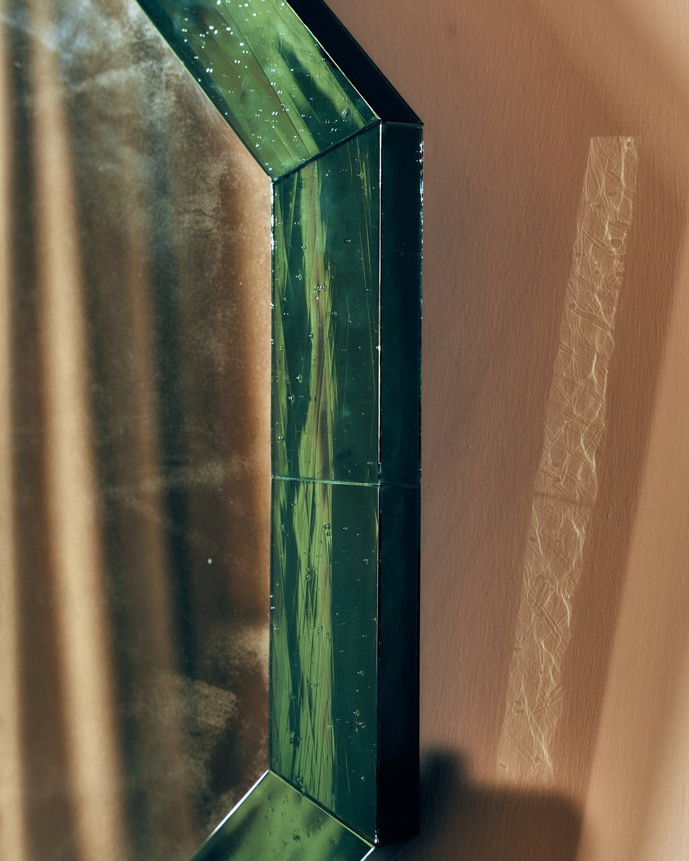 Close-up of green mirror glass frame on a beige wall.