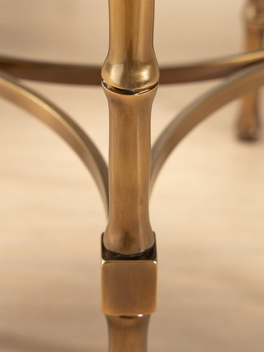 Close-up of a brass side table base with a beige background.