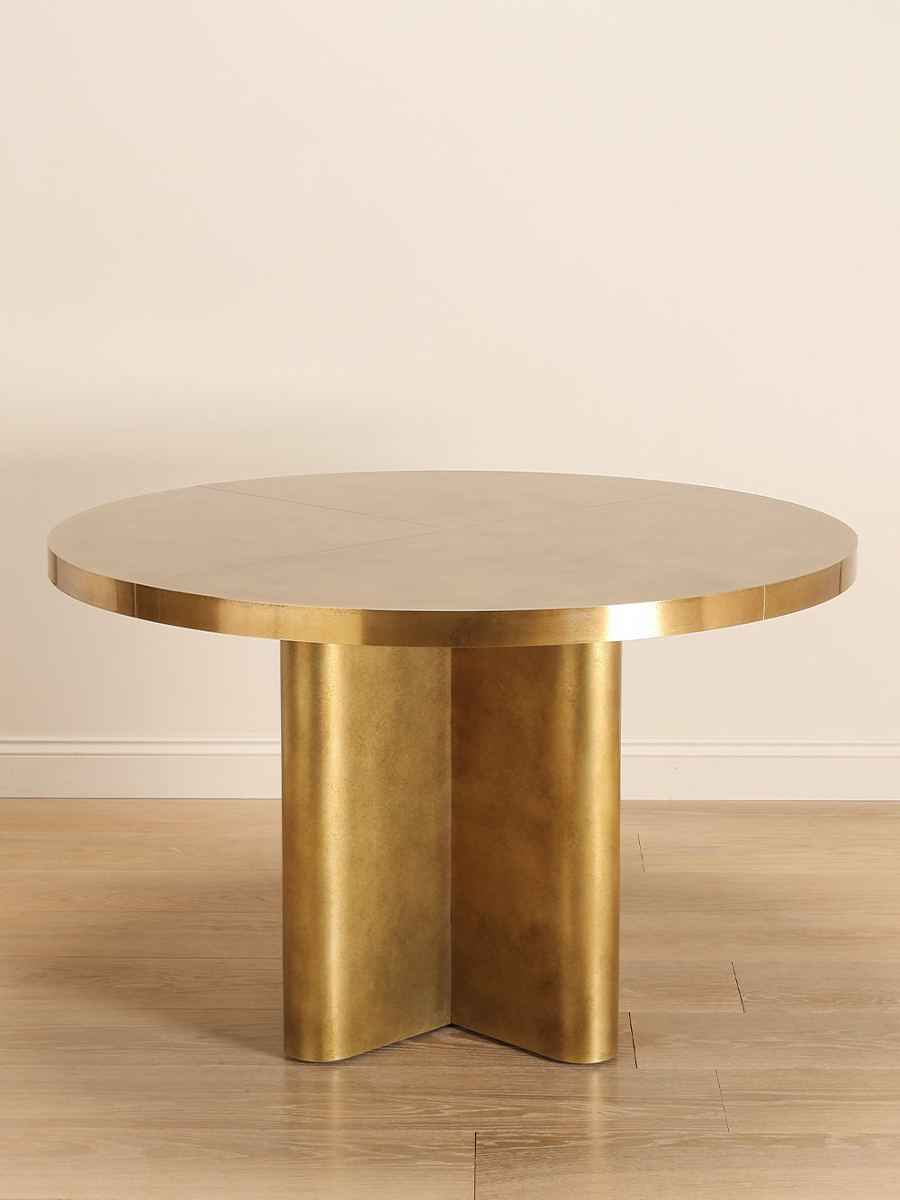 Brass round table with a unique geometrical base design on a wooden floor.
