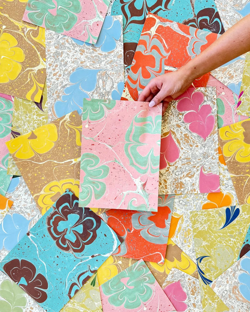 Colourful marbled wallpaper sheets with a hand holding one sheet against a background of various marbled patterns.