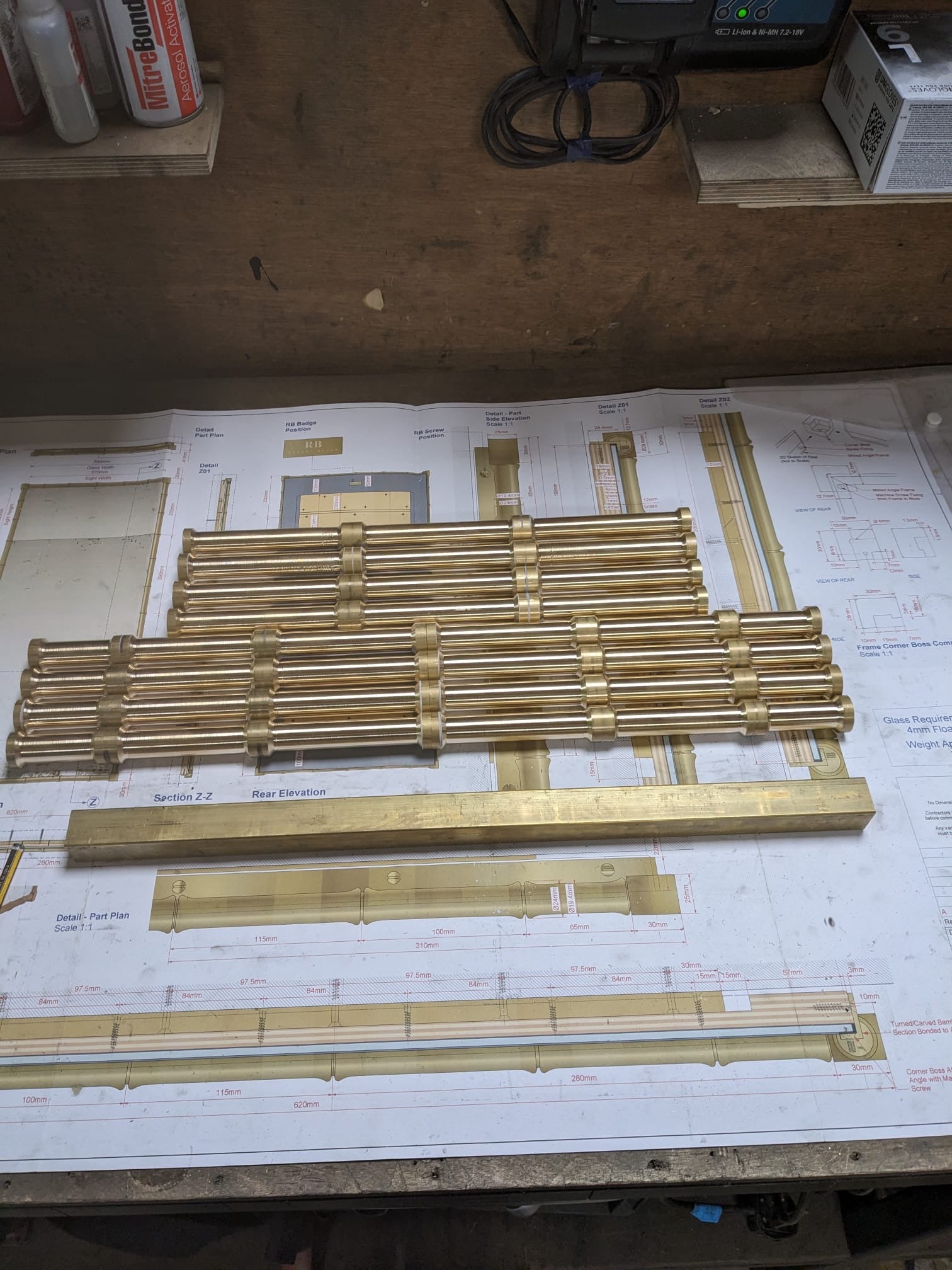 Gold metal bars on a workbench with design drawings in the background.