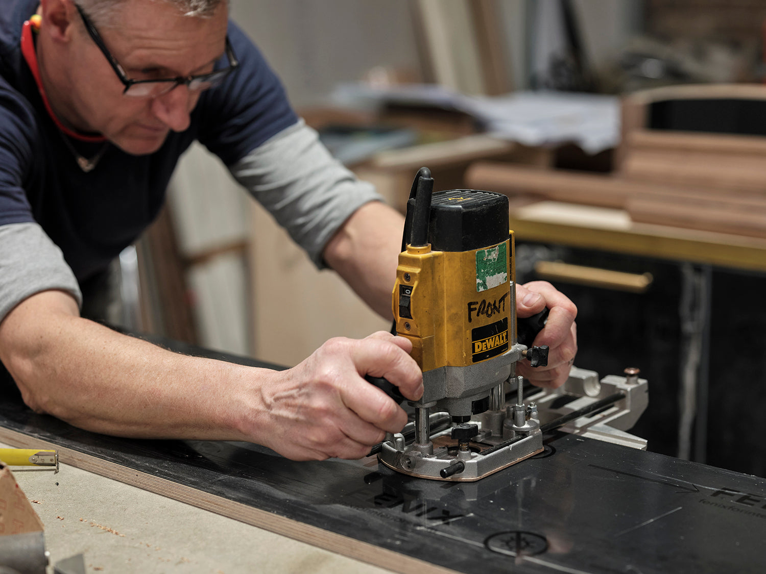 Man using a Dewalt router on a workbench in a workshop setting.